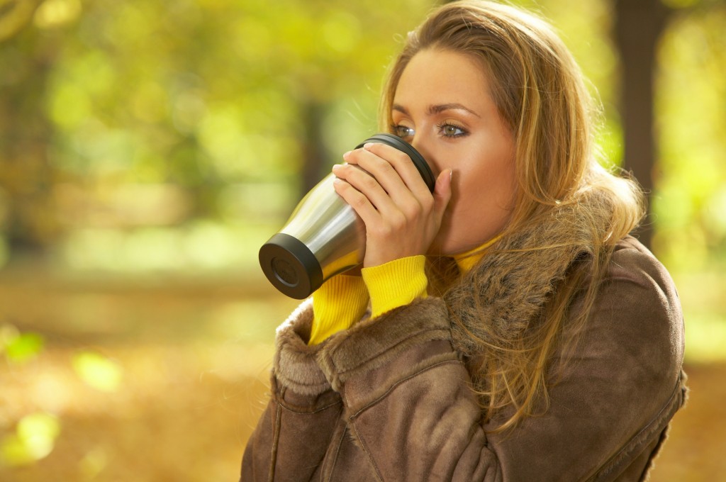 A woman outside in the fall weather drinking coffee