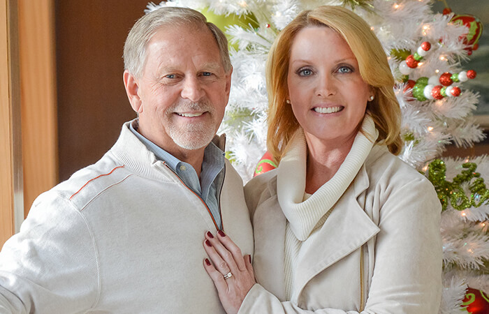 An older couple standing next to christmas tree