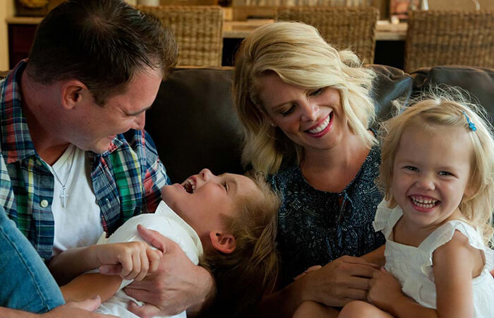 A mom and dad playing with their son and daughter on the sofa