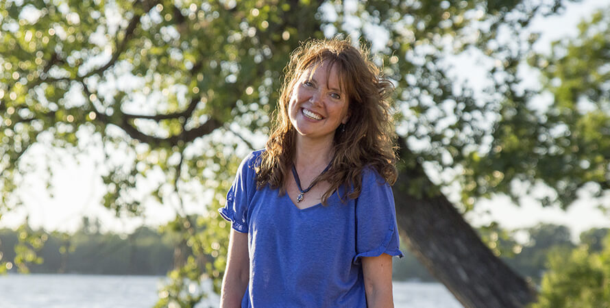 A brunette woman smiling in front of a tree on a sunny day