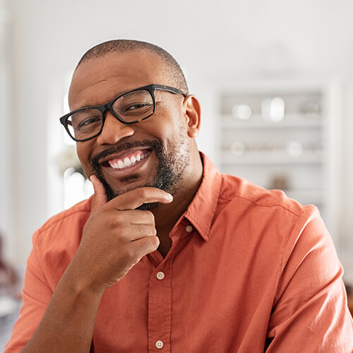 A man with glasses holding his face while smiling into the camera